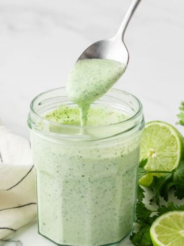 jar filled with homemade cilantro lime sauce and a spoon drizzling some sauce to show creamy texture