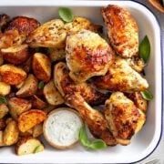 baked chicken pieces in a baking tray with potatoes and dipping sauce