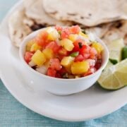 small white bowl of pineapple salsa on a plate with tortillas and a lime wedge