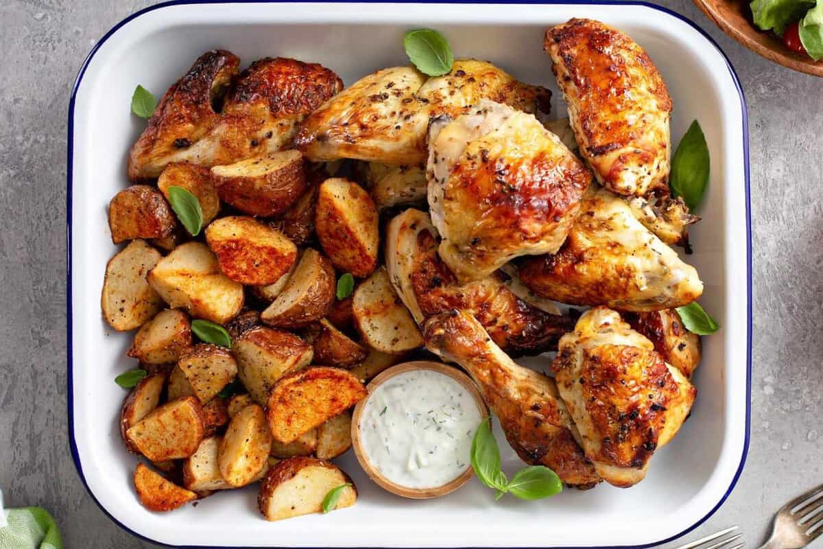 baked chicken pieces in a baking tray with potatoes and dipping sauce