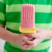 pink yogurt popsicle being held by a child wearing a striped green shirt