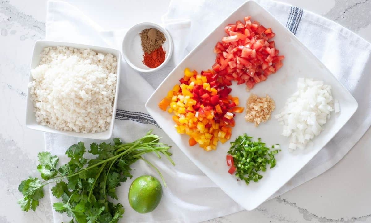 Ingredients for Mexican cauliflower rice, including cauliflower rice, tomatoes, bell peppers, onion, garlic, jalapeño, cilantro, lime, and spices.