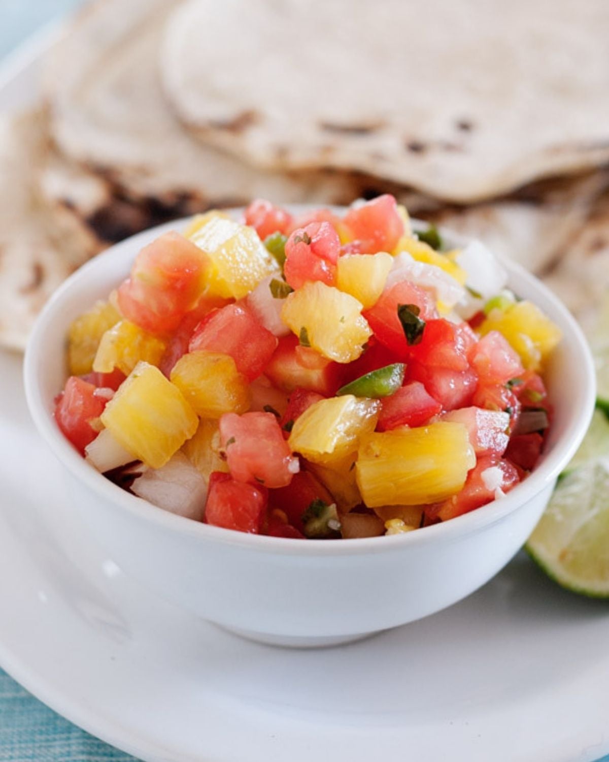a small bowl with pineapple salsa and some tortillas in the back
