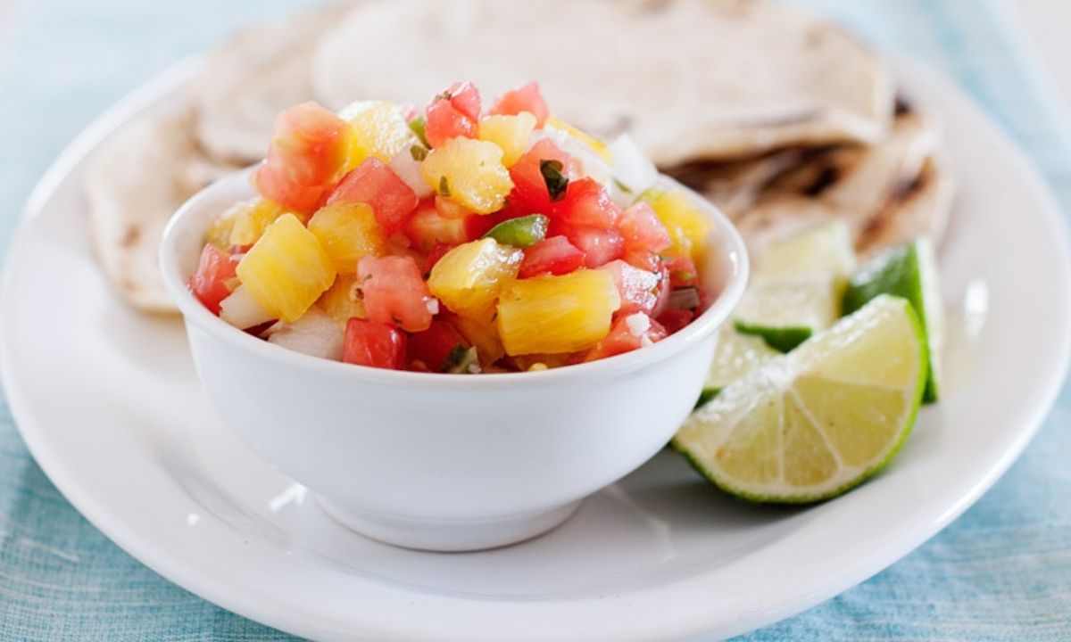 a small bowl with pineapple salsa surronded by tortillas and lime wedges