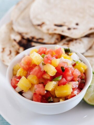 a small bowl with pineapple salsa and some tortillas in the back