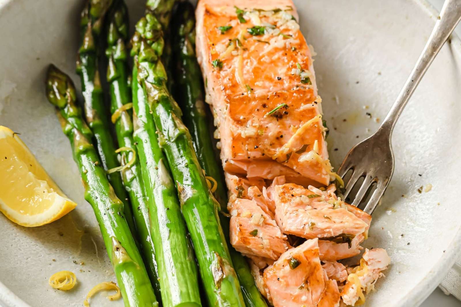 a salmon fillet serve on a dish with asparagus and a lemon wedge