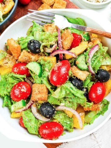 side salad with lettuce, tomato, olives, onion, and croutons in a white dish