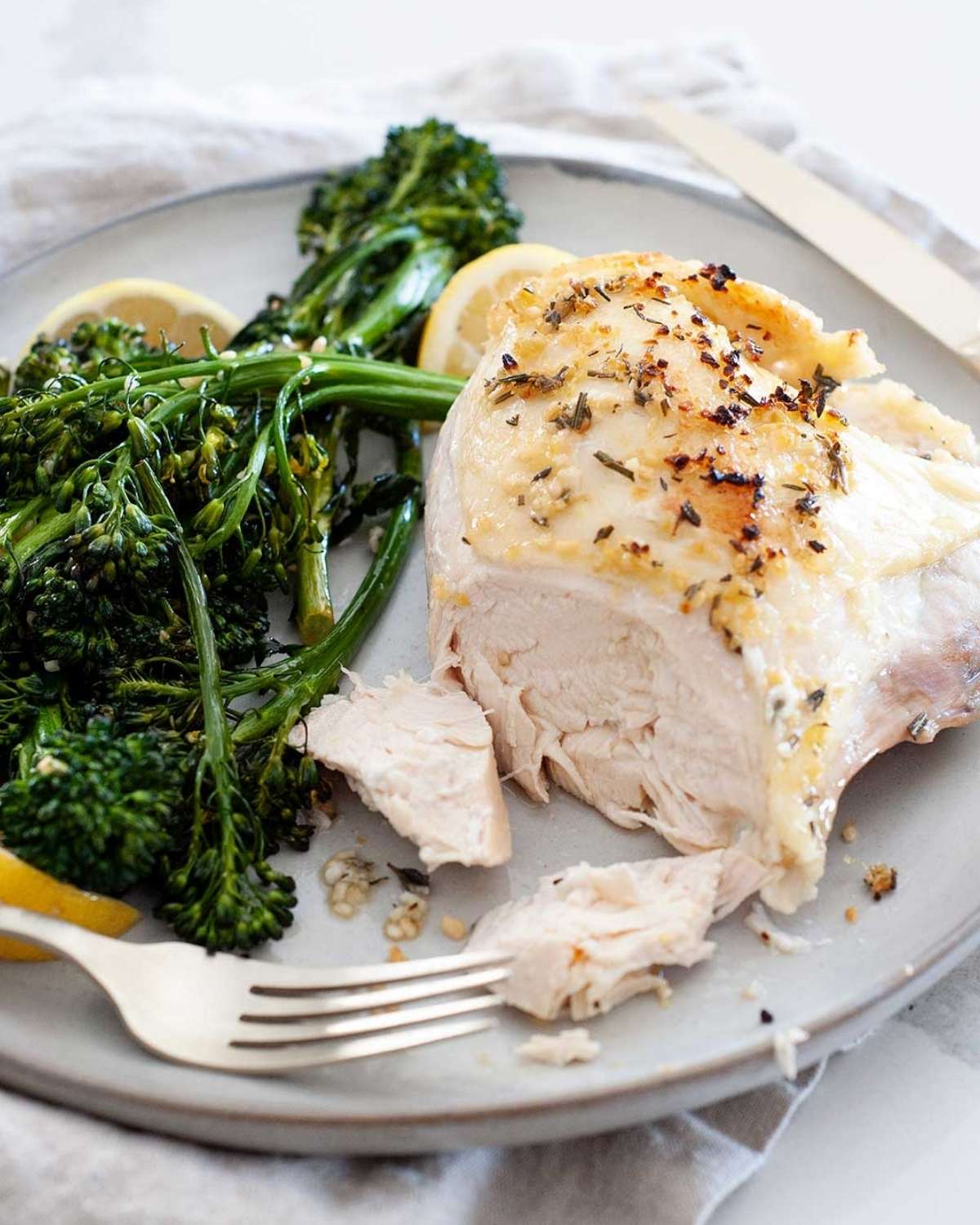 chicken breast with broccolini and lemon in a white dish