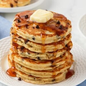 fluffy stack of chocolate chip pancakes topped with a pat of butter and pancake syrup on a plate