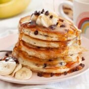 stack of fluffy chocolate chip pancakes with banana slices and syrup
