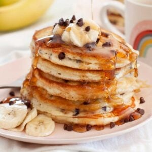 stack of fluffy chocolate chip pancakes with banana slices and syrup