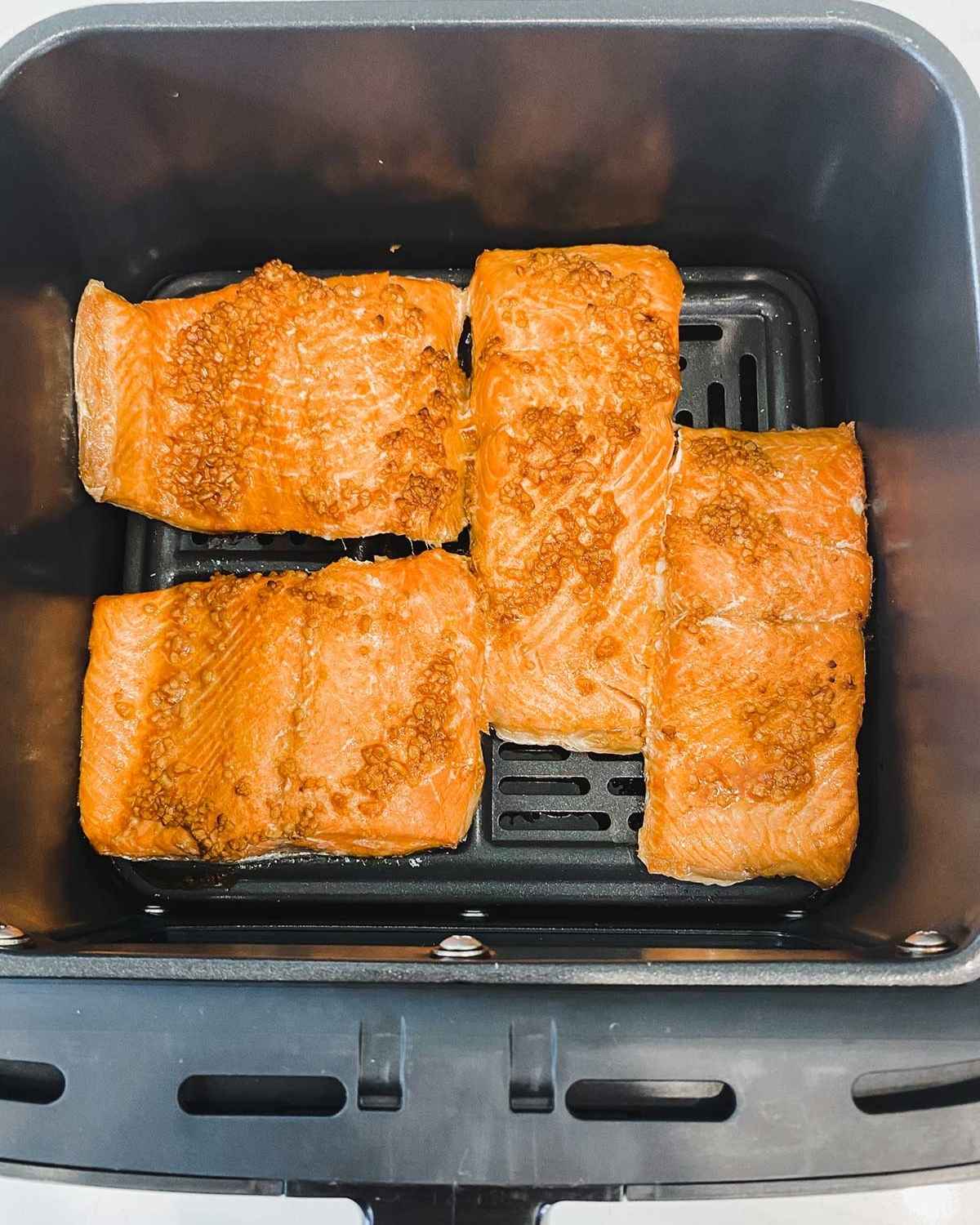 air fryer basket with four salmon pieces