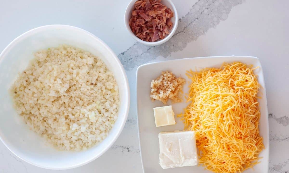 Ingredients to make cheesy cauliflower rice: cauliflower rice, butter, garlic, cream cheese, cheddar cheese, and bacon bits