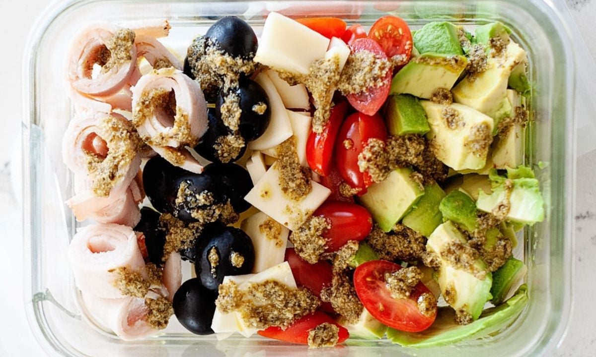 pesto salad with avocado, tomatoes, olives, ham and cheese in a glass lunch container