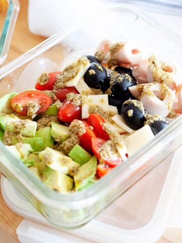 pesto salad with avocado, tomatoes, olives, ham and cheese in a glass lunch container