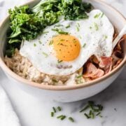 a bowl of savory oatmeal with a fried egg, bacon and veggies