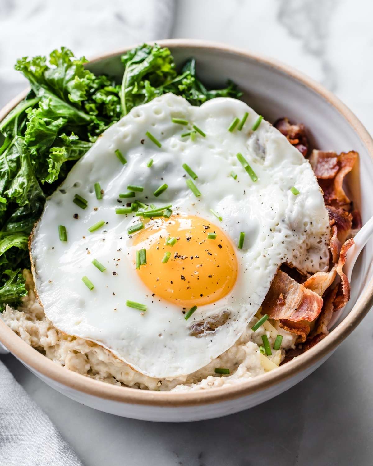 a bowl of savory oatmeal with a fried egg, bacon and veggies