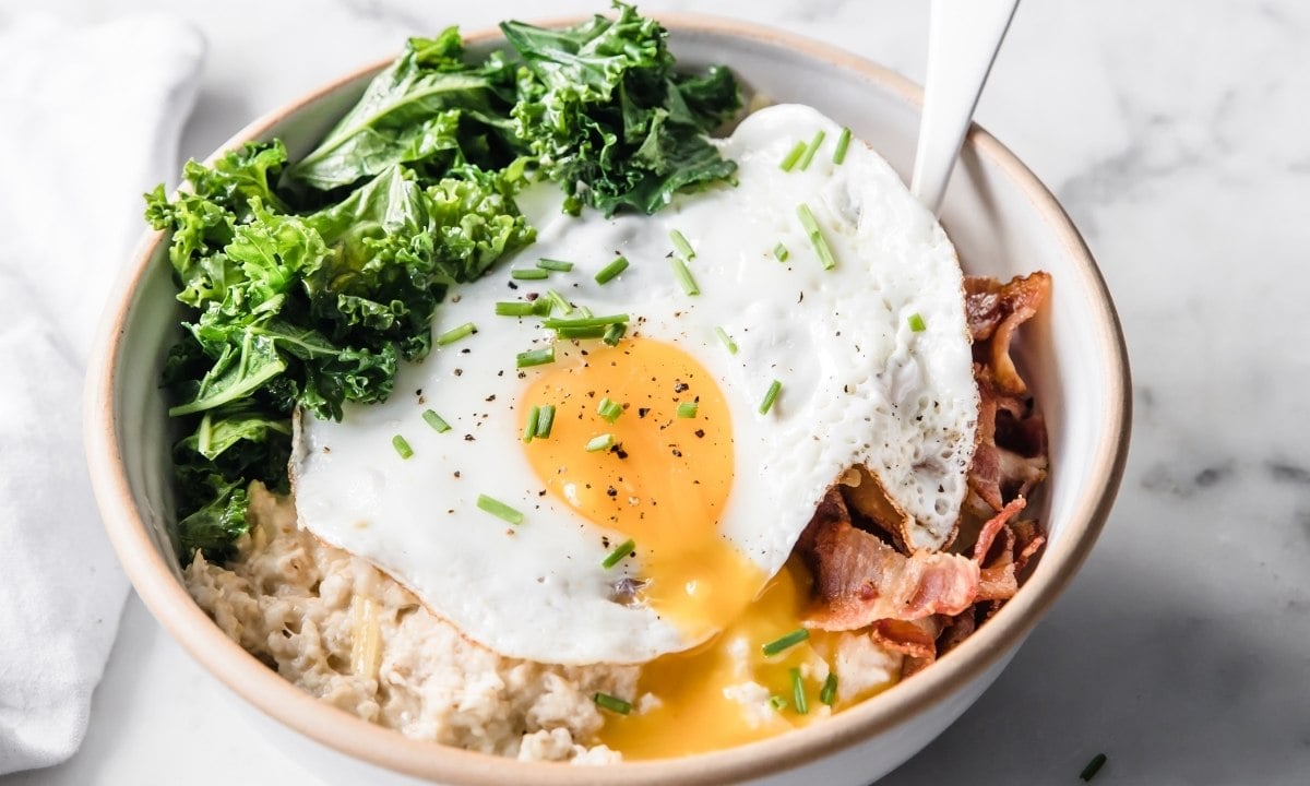 a bowl of savory oatmeal with a fried egg, bacon and veggies