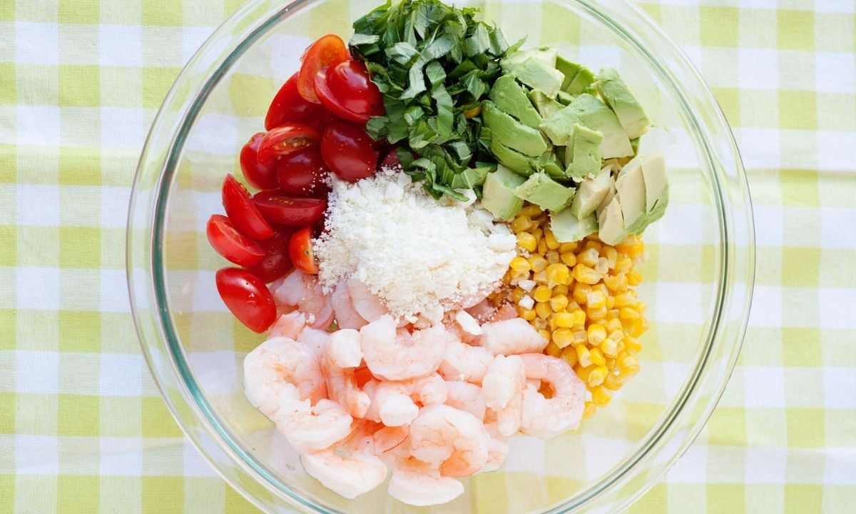 a bowl with shrimp, tomato, corn, diced avocado, cheese, and basil