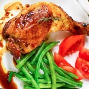 chicken leg quarter on a plate with green beans and tomatoes
