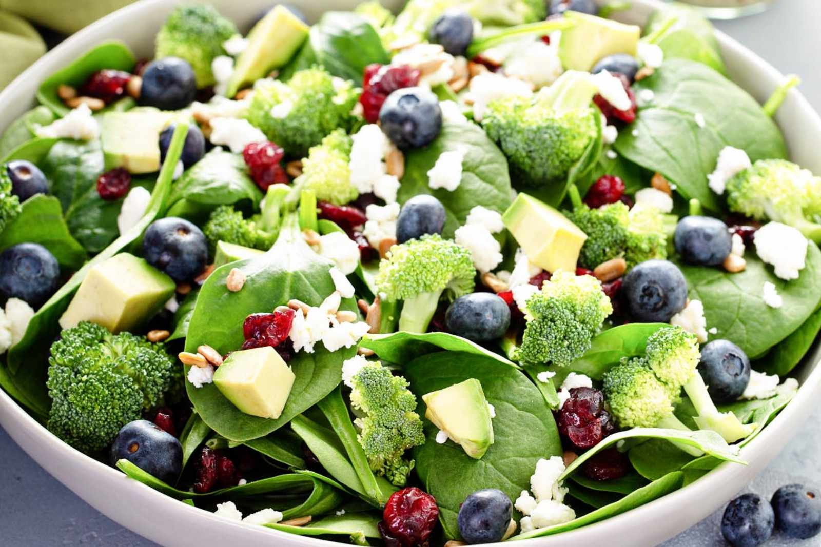 blueberry spinach salad with broccoli and avocado in a large bowl