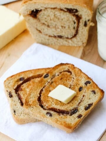 loaf of cinnamon raisin bread with two slices cut out topped with butter