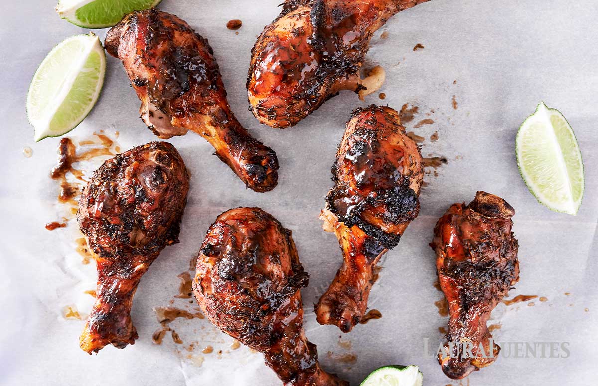 jerk chicken drumsticks on a baking sheet with lime wedges