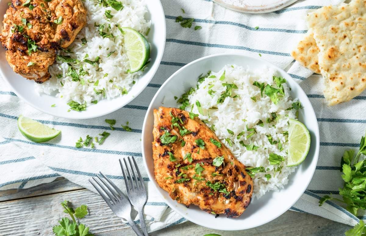two plates with chicken breast, rice, and lime slices