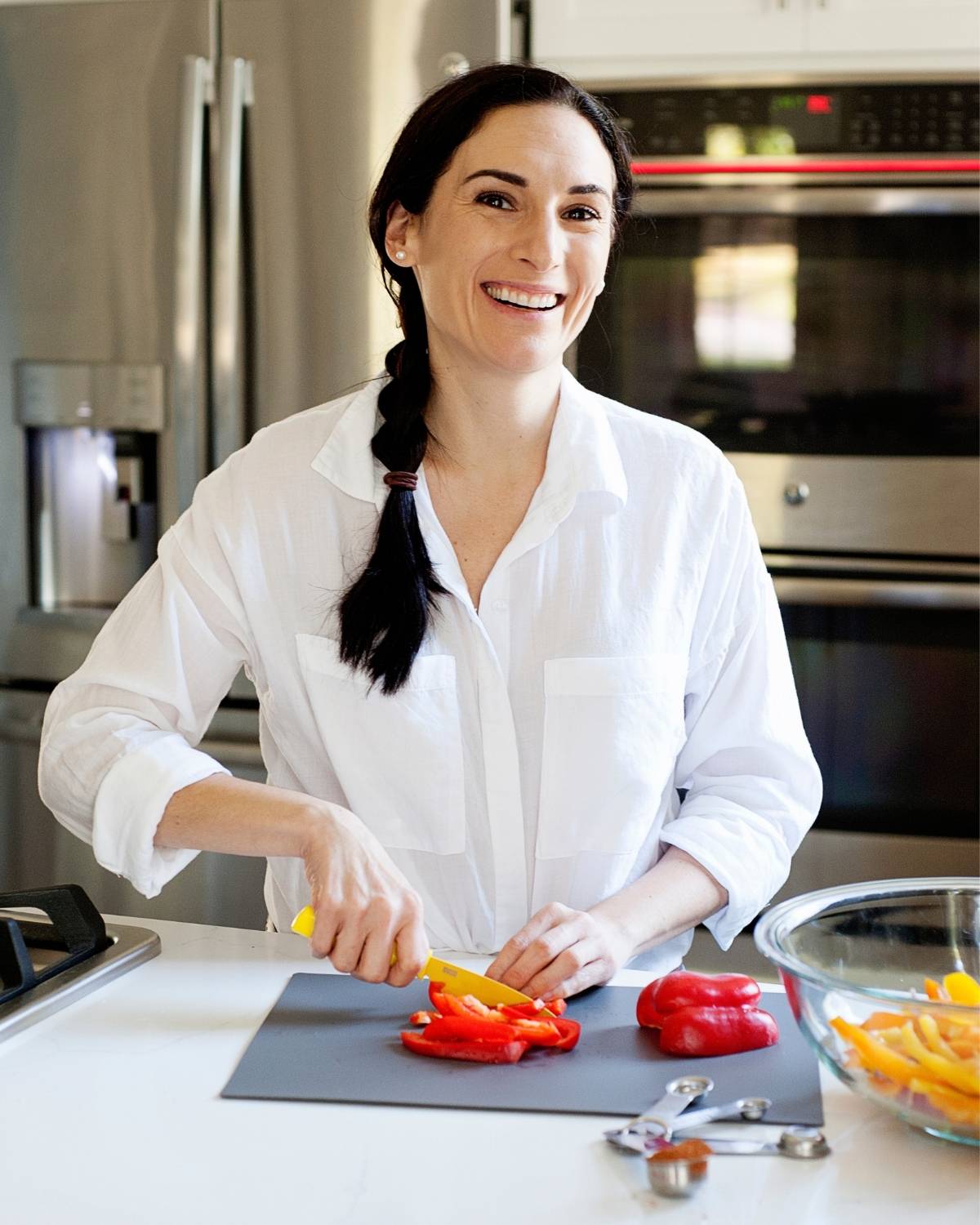 Laura standing in kitchen cutting red bell peppers into slices