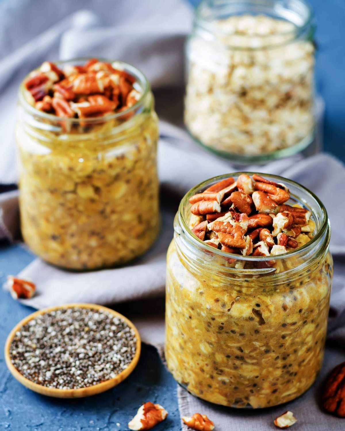 two jars of pumpkin pie overnight oats, a little bowl of chia seeds on the side, and a jar with oats behind