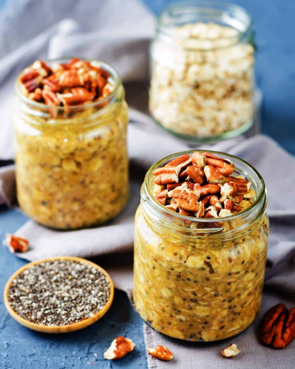 two jars of pumpkin pie overnight oats, a small bowl of chia seeds on the side, and a jar with oats at the back
