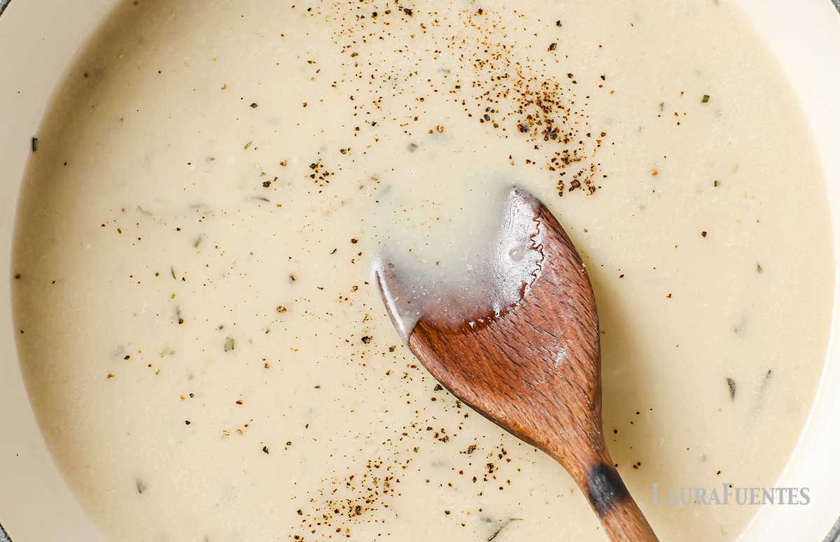 large pot of creamy garlic sauce with a wooden spoon