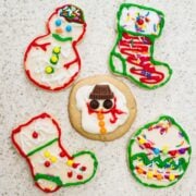 five sugar cookies decorated as snowman, santa boots, and christmas ball