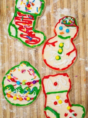 four sugar cookies decorated as snowman, santa boots, and christmas ball