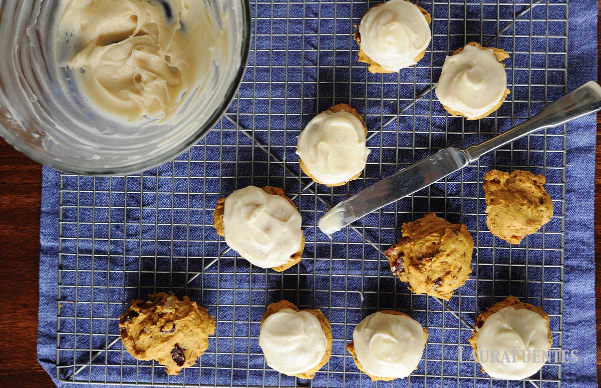 pumpkin cookies being frosted with cream cheese icing