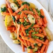 overhead view of a large serving dish of carrots, peas and potatoes