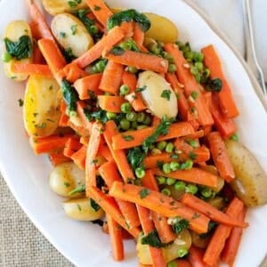 overhead view of a large serving dish of carrots, peas and potatoes