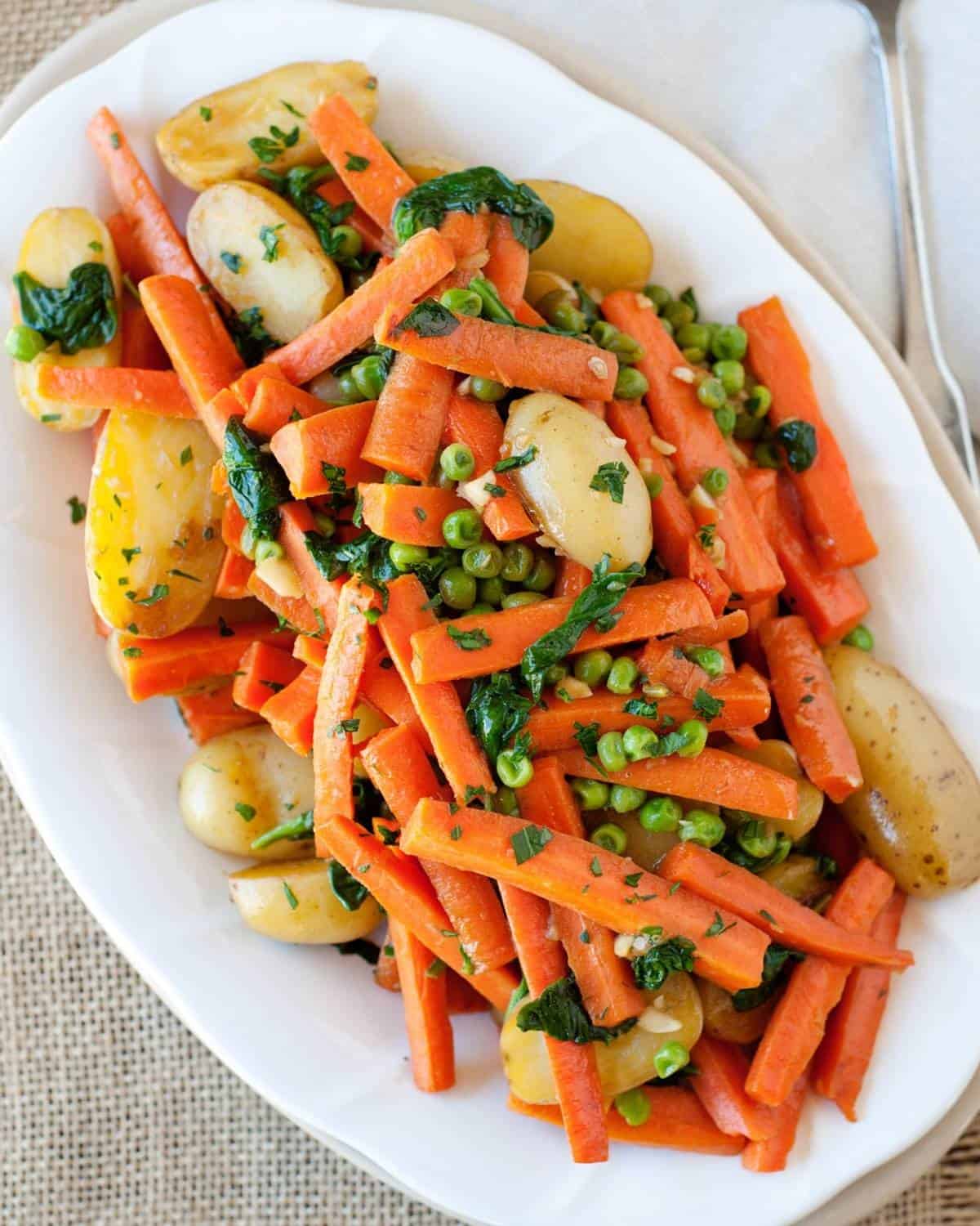 overhead view of a large serving dish of carrots, peas and potatoes