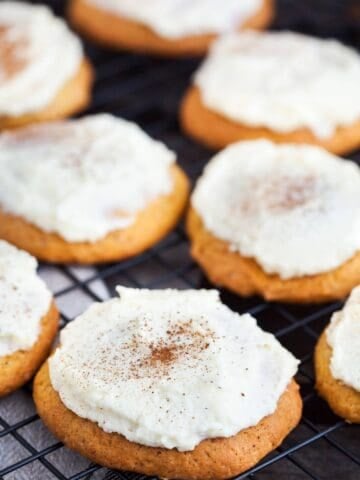 pumpkin cookies with cream cheese frosting sitting on a wire rack