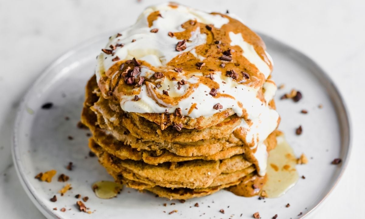 Stack of peanut butter pancakes topped with whipped cream and more peanut butter on top.