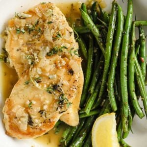 garlic chicken breast on a plate with green beans and a lemon wedge