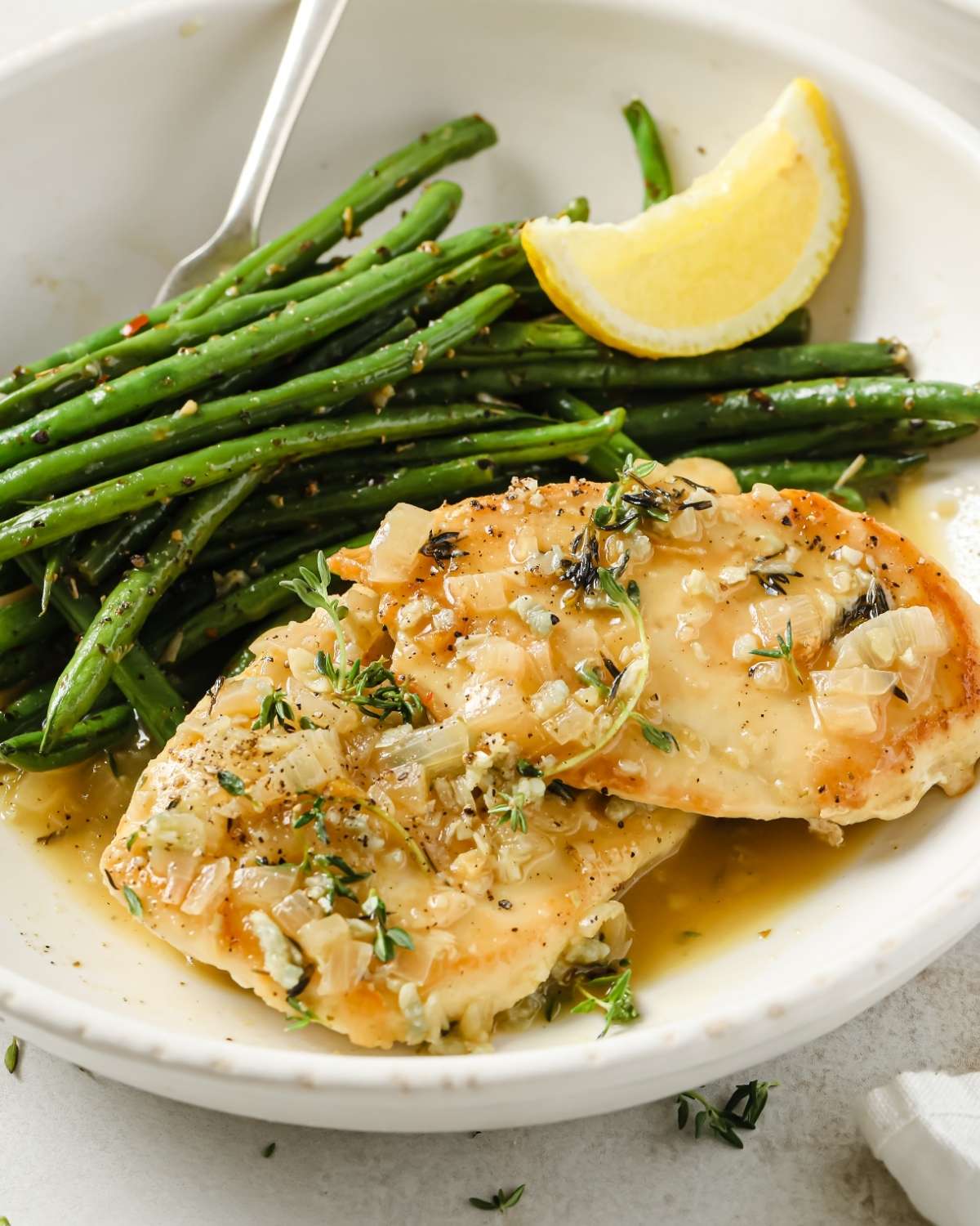 garlic chicken breast on a plate with green beans and a lemon wedge