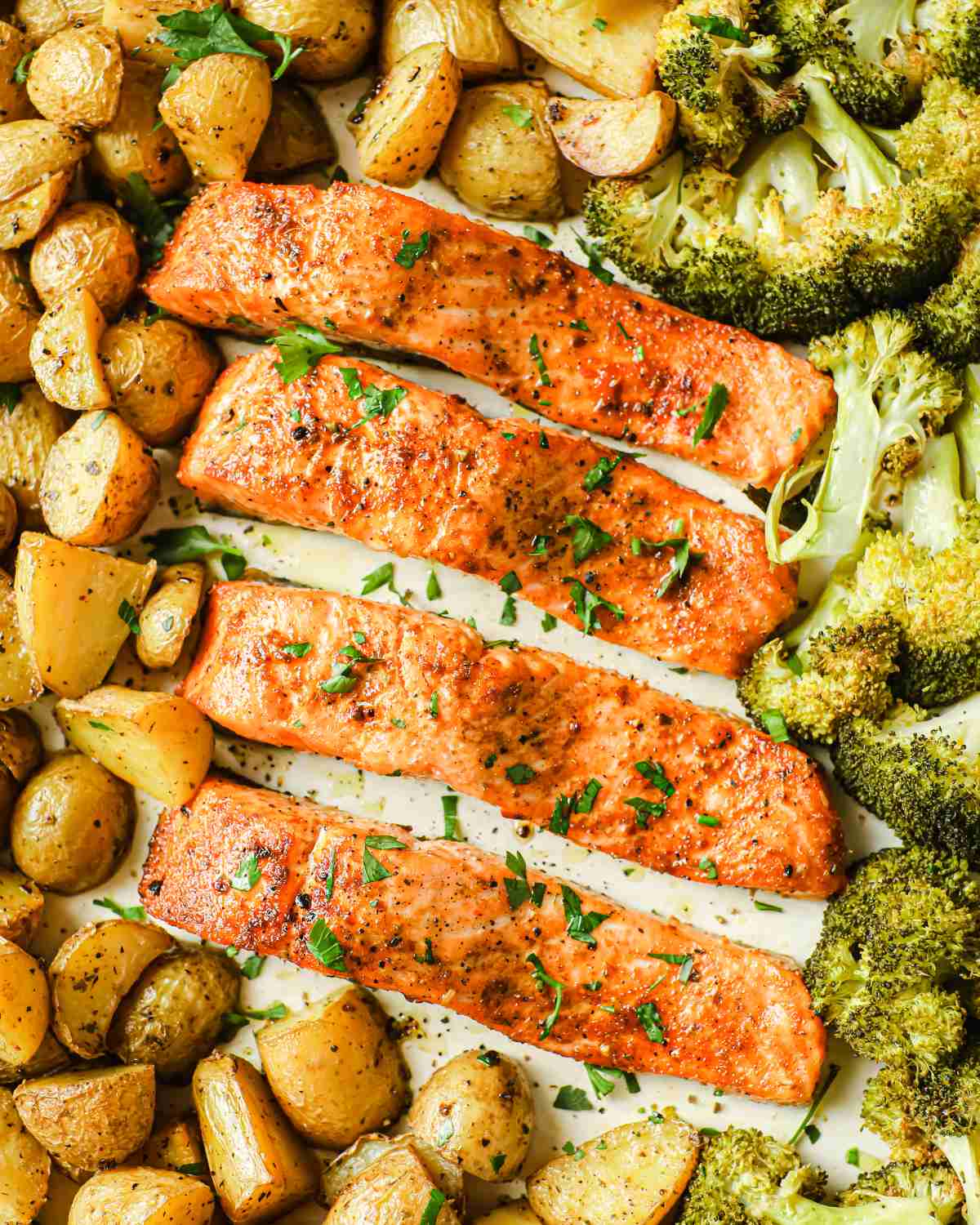 overhead view of baked salmon and potatoes on a sheet pan with broccoli too