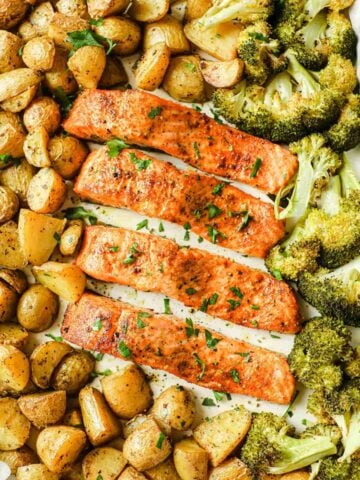 overhead view of baked salmon and potatoes on a sheet pan with broccoli too