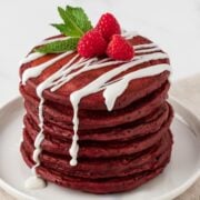 stack of fluffy red velvet pancakes on a plate with a light drizzle of white sugar glaze topped with raspberries