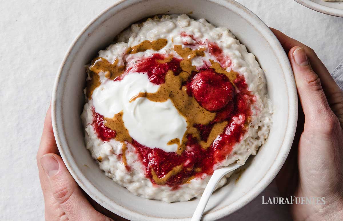 a hand holdin a bowl of oatmeal topped with fruit and greek yogurt