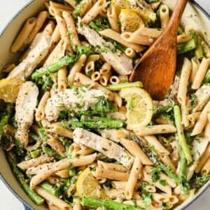 a skillet with asparagus chicken pasta and a wooden spoon