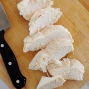 Sliced poached chicken breasts on a cutting board with a knife