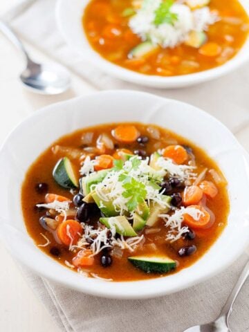 vegetable soup with black beans and zucchini in a bowl and another soup in the back