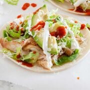 closeup of spicy chicken taco with avocado slice on top